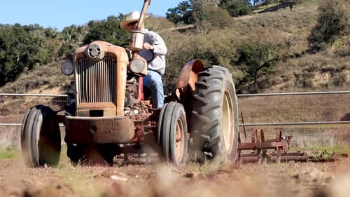 Rancher Driving Tractor with Harrow Plowing Field Rack Focus to Tractor