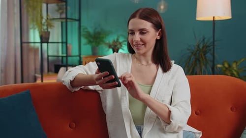 Young Woman Uses Smartphone on Orange Couch