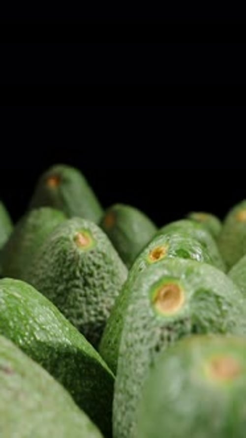 Vertical video. Green avocados neatly arranged on a table against a black background. Dolly slider,