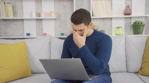 Hombre infeliz que trabaja con una computadora portátil en casa.