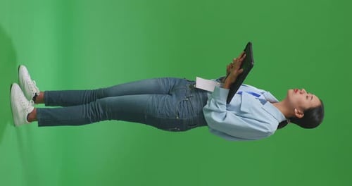 Side View Of Full Body Asian Woman Using Tablet An Looking Around On Green Screen In The Studio