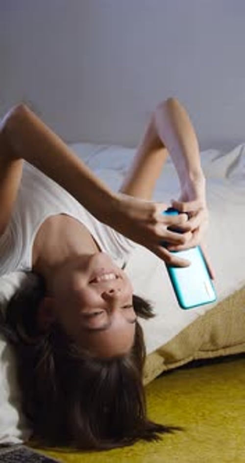 Teen Smiles, Uses Smartphone While Lying on Bed