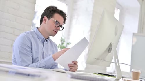 Attractive Working Young Man Reading Documents in Office