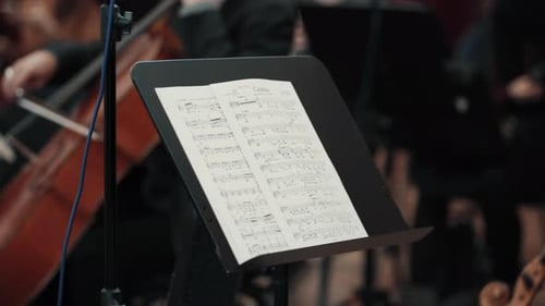 Sheet music on a stand with musicians playing in the background