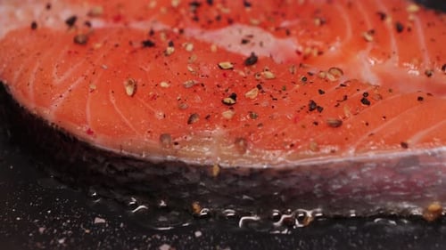 Close-up of appetizing juicy salmon steak sprinkled with black allspice frying in a pan.