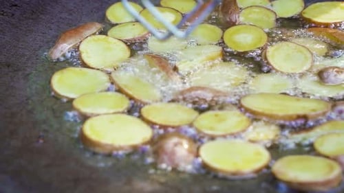 Selective focus shot of frying potatoes over the open fire, handheld.