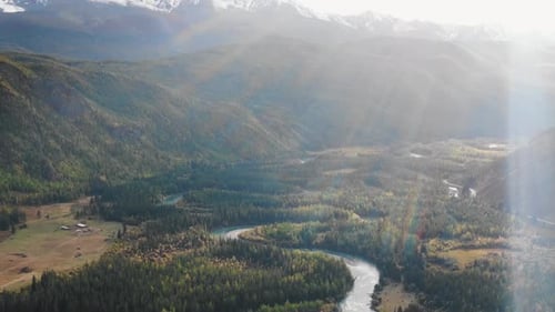 Sunlit Aerial View of a Meandering River Through a Forested Mountain Valley
