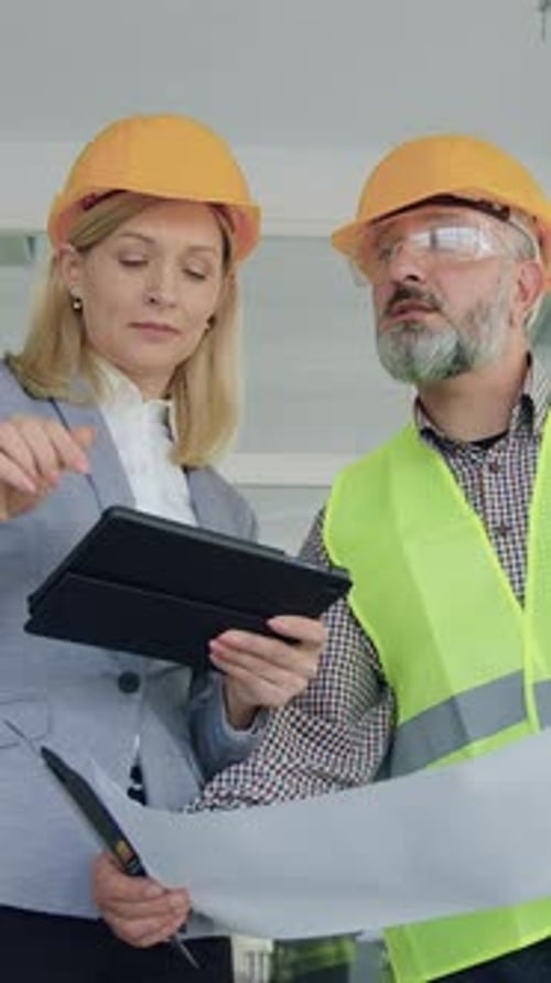 Architects Reviewing Blueprints and Tablet in Construction Site