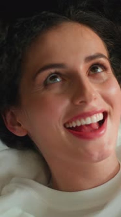 Gros plan d'une femme heureuse caucasienne souriante regardant la caméra jouant avec des cheveux bouclés couchée dans son lit à