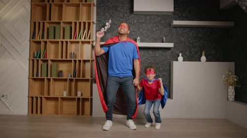 Father and Son in Superhero Costumes Playfully Jumping
