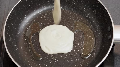 Close-up shot wet pancake batter being poured into a metal pan with Oil Top View