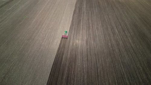 Aerial View of a Tractor Plowing a Large Field Creating Distinct Patterns in the Soil Agricultural