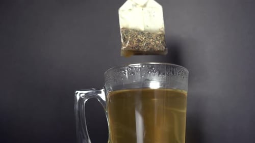 Heißer dampfender Tee wird in einem Glas vor dunklem Hintergrund zubereitet und gebrüht. Männliche Hand, die den hält