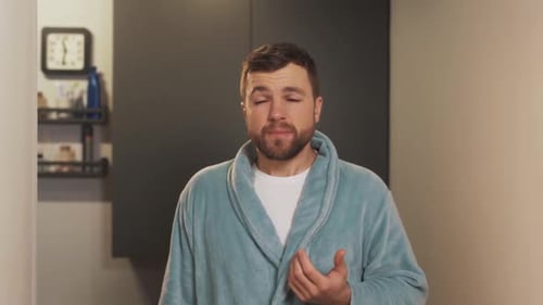 un jeune homme tousse devant un miroir et utilise un spray pour la gorge