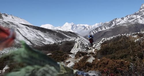 Person walking along the trail in Nepal carrying large bag with mountains in the distance.