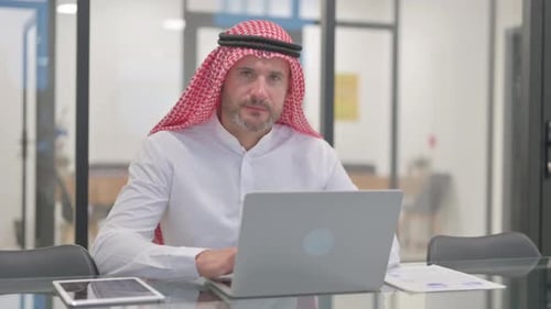 Arab Man Smiling at Camera while Working on Laptop in Office