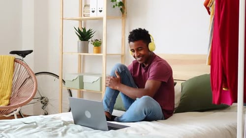 Young Man Using Laptop in Bedroom with Headphones