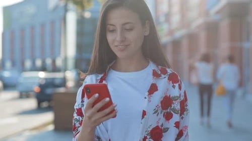 Smiling woman uses her phone on a city street