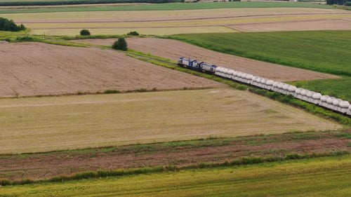 Modern freight train with industrial cargo moves through rural Poland, aerial view