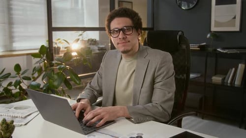 Porträt eines lächelnden Geschäftsmannes der Generation Z, der am Schreibtisch am Laptop arbeitet