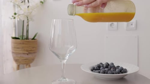 Versez à la main du jus d'orange frais dans un verre sur la table de la cuisine, myrtilles sur une assiette, dans un style moderne et lumineux