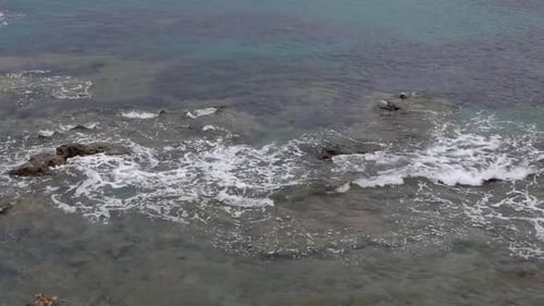 Small waves gently breaking over flat rocks on the shoreline. Sicily. Italy.