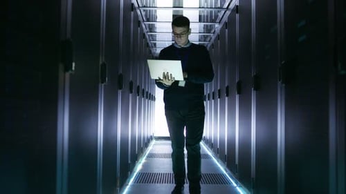 Un
ingeniero de servidores masculino recorre con un portátil abierto las filas de servidores en rack. Está trabajando en Big,