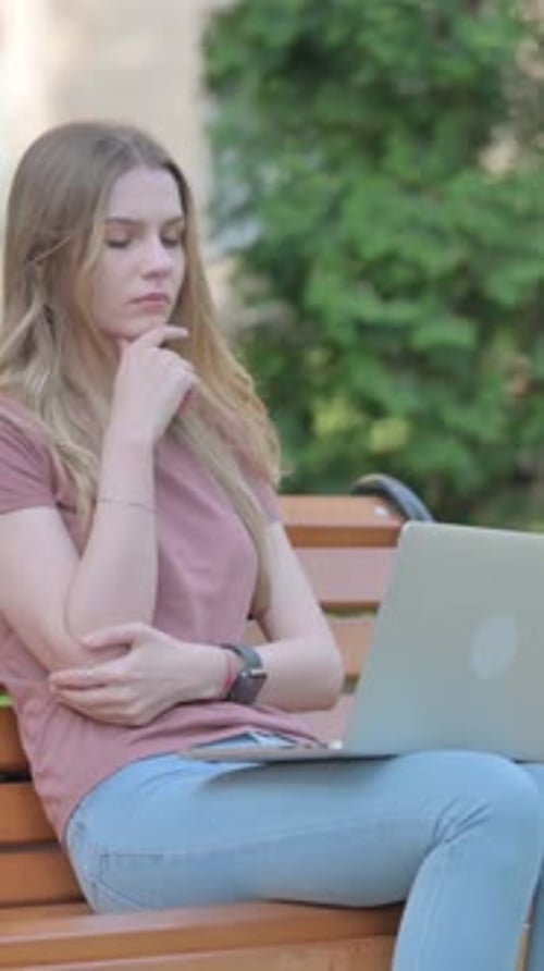 Woman Shocked by Loss on Laptop while Sitting Outdoor on a Bench, vertical