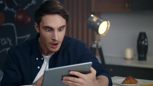Surprised businessman gets good news on tablet computer at home office