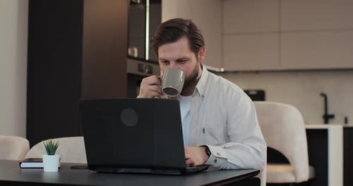 Man Working on Laptop and Drinking Coffee at Home