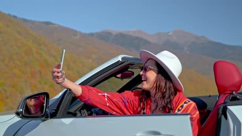 Glückliche Frau macht Selfie im Cabrio in wunderschöner Berglandschaft an einem sonnigen Tag