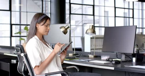 Using digital tablet, businesswoman working at modern office desk with computer