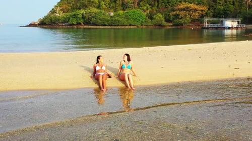 Two girls in bikini sunbathe on paradise beach with white sand washed by calm clear water of lagoon