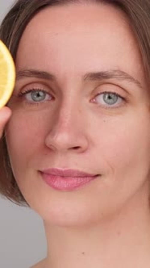 Woman Holding Orange Slice to Eye in Studio