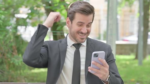 Excited Businessman Celebrates Good News on Smartphone Outdoors