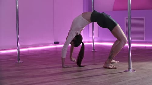 Woman Performing Backbend and Leg Raises Near Pole in Dance Studio