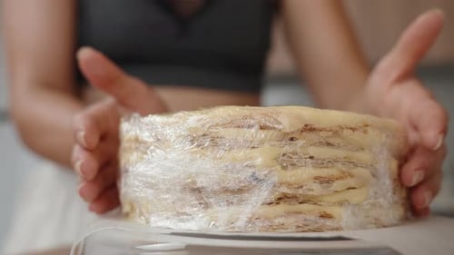 The woman wraps the Napoleon cake layers with cream in plastic wrap.
