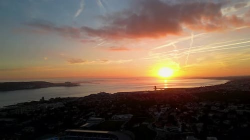 A spectacular aerial view of a sunset over the ocean with a coastal city in the foreground