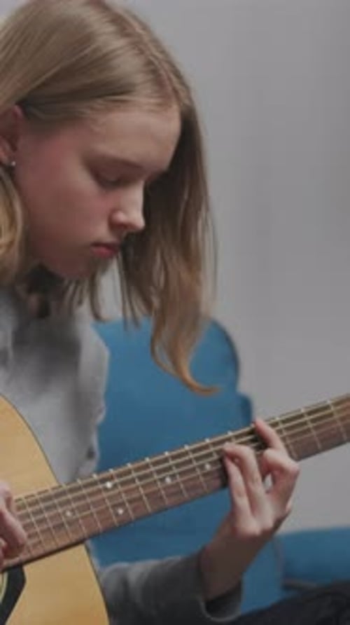 Thoughtful Teenager Practicing Acoustic Guitar at Home Focusing on Chords and Finger Placement While