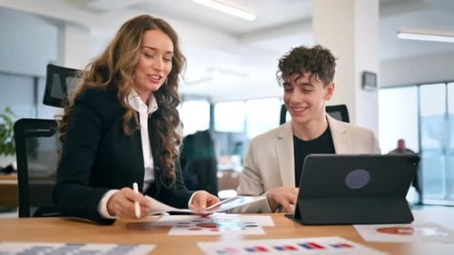 Business session in an office. Woman and a young man discussing business affairs. Gadgets with graph