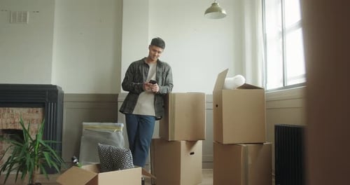 Mid Adult Male Standing in New Home using Smartphone surrounded by Boxes