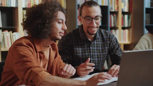 Young Male Group Mates Discussing Homework on Laptop in Library