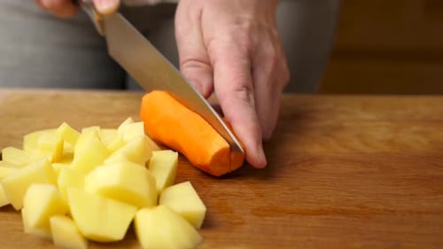Woman Cuts Carrot on Board in Kitchen
