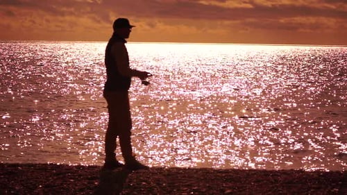 Mann steht auf dem Pier und hält eine Angel in der Hand und bereitet sich darauf vor, sie bei warmem Sonnenuntergang ins Meer zu werfen