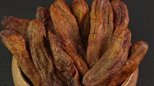 Small dried bananas spinning in a wooden bowl close up. Sweet dried fruits made from dehydrated