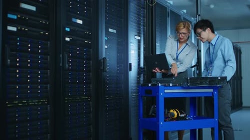 In the Modern Data Center: Female Engineer and Male IT Specialist Work with Server Racks, Discussin