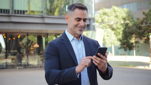 Smiling Man Uses Phone Outside Modern Building
