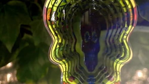 Hypnotic metal sugar skull decorative colourful spinning garden ornament hanging from tree closeup s