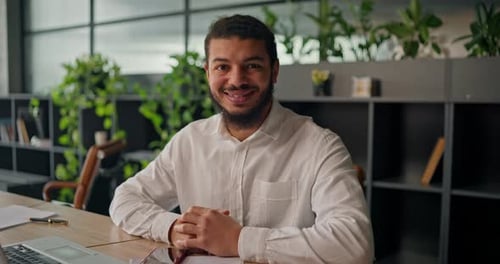 A Portrait of an African Office Worker in a White Business Shirt Sitting at a Table and Smiling