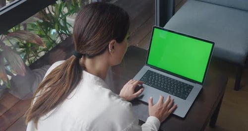 Successful Businesswoman Sitting at Cafe Table Working on Green Screen Laptop at Modern Coffeehouse